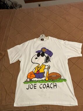 Peanuts White T-Shirt with Purple, Yellow and Black Snoopy Coach Graphic.
